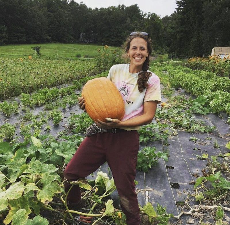 a female farmer holding a large orange pumpkin in a field